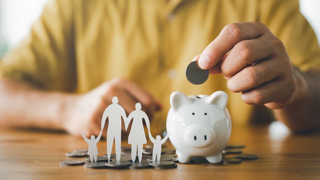 A hand putting money into a piggy bank with a family nearby.