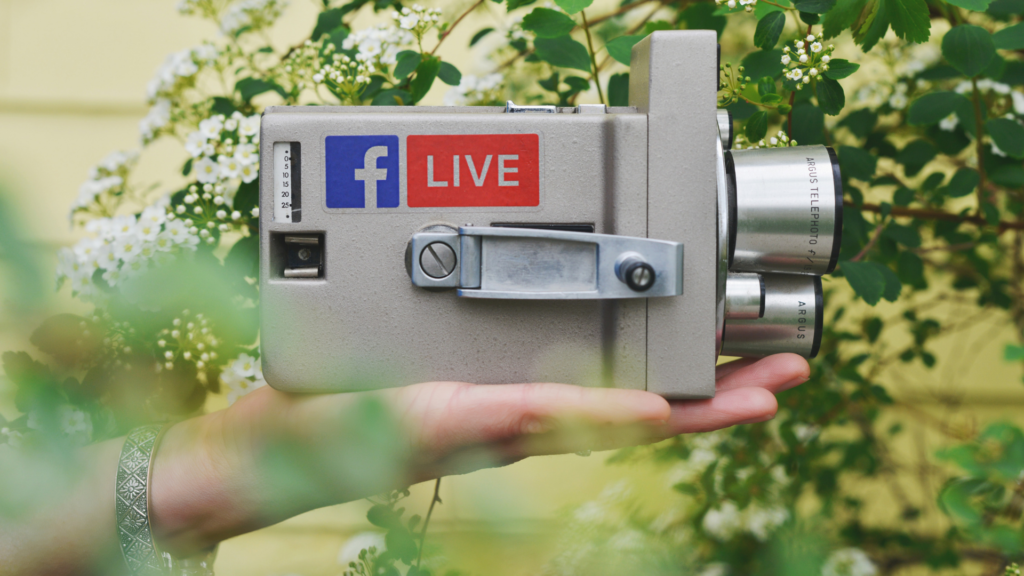 a hand holds a film camera with a Facebook Live sticker on it