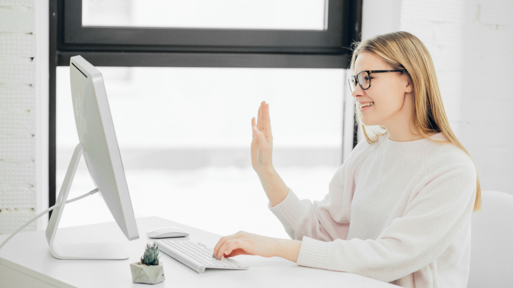 Saleswoman smiles and waves at her computer webcam